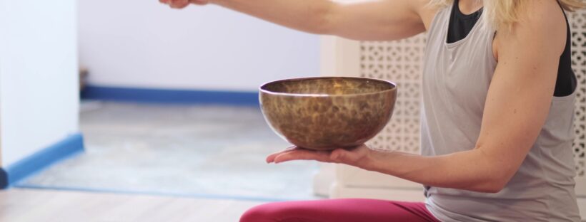 Woman playing on Tibetan singing bowl while sitting on yoga mat. Vintage tonned.